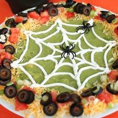 a spider web cake with black olives, tomatoes and guacamole on it