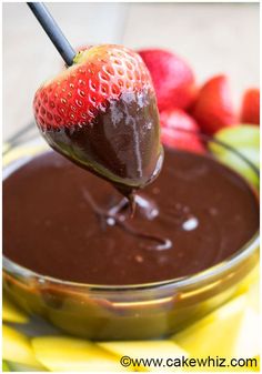 a chocolate covered strawberry being dipped into a bowl full of strawberries and other fruit