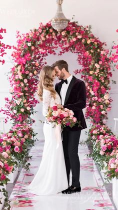 a bride and groom standing in front of an archway with pink flowers on the floor