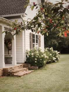 a white house with steps leading up to the front door and flowers growing on the lawn