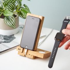 a person holding a cell phone and charging it on a wooden stand next to a plant