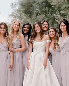 a group of women standing next to each other in long gray dresses with one woman wearing a white dress