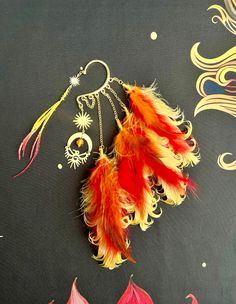 This vibrant sun fire phoenix feather ear wrap is sure to make a statement and bring out your inner magic!

Gold ear cuff features brass phoenix bird, moon connector, and sun pendants, yellow and red crackled glass bead, and hand wire wrapped red, orange, and yellow feathers all hanging from gold plated chains.

This feather ear wrap is perfect for adorning pierced and non-pierced ears and is lightweight to wear!

Your ear wrap is shipped in an organza jewelry bag, ready to be the perfect unique gift for yourself or someone you love! ❤️‍🔥 Flame Accessories, Unique Ear Cuffs, Organza Jewelry, Feather Ear Cuff, Phoenix Feather, Phoenix Jewelry, Feather Headpiece, Yellow Feathers, Phoenix Art