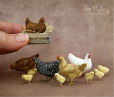 a hand holding a tiny toy chicken in front of small chickens