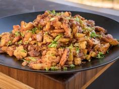 a black plate topped with fried food on top of a wooden table