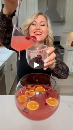 a woman is pouring some liquid into a bowl filled with oranges and cranberries