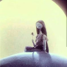 a doll sitting on top of a blue object with a flower in it's hand