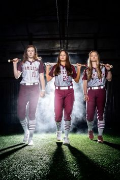 three girls in baseball uniforms are holding bats