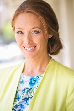 a woman wearing a yellow jacket and blue flowered shirt smiling at the camera with her eyes closed