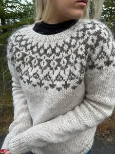 a woman wearing a white sweater and blue jeans is standing in front of some trees