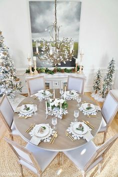 a dining room table set for christmas with white plates and silverware on the place settings