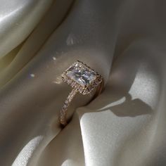 an engagement ring on top of a white satin fabric with the light shining through it