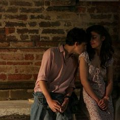 a young man and woman sitting next to each other in front of a brick wall