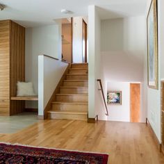 an empty living room with wooden floors and white walls, stairs leading up to the second floor