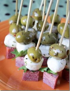 small appetizers with olives and meat on skewers are displayed on an orange plate