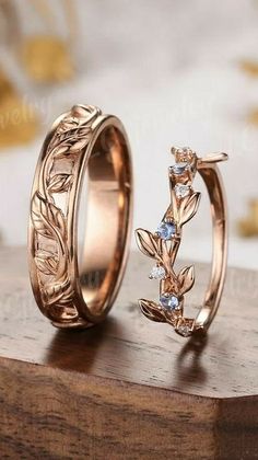 two gold wedding rings with leaves and blue topazs on them sitting on a wooden surface