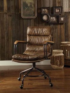 a brown leather office chair sitting in front of a wooden wall with pictures on it