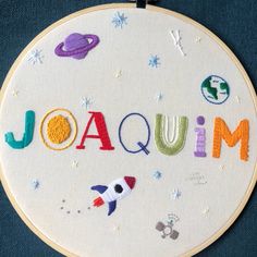 embroidered name art with space theme displayed on blue cloth wall hanging in circular wooden frame