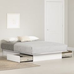 a white bed with drawers underneath it in a room next to a door and rug on the floor