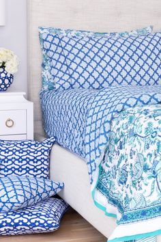 a bed with blue and white comforters on top of it next to a night stand