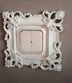 a white light switch sitting on top of a wall next to a gray wall with an ornate frame