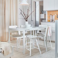 a white dining table and chairs in a room with beige curtains on the windowsill