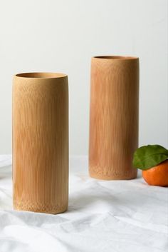 two wooden vases sitting next to each other on a white table cloth with an orange in the background