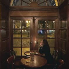 a woman sitting at a table with a candle in her hand looking out the window