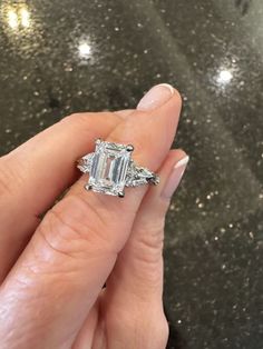 a woman's hand holding an emerald and diamond ring on top of her finger