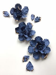 three blue flowers on a white surface next to each other with gold trimmings