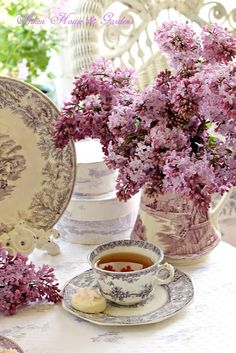 a tea cup and saucer on a table with lilacs