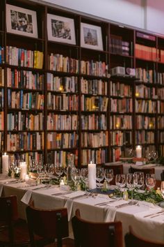 the long table is set for dinner in front of bookshelves with candles on them