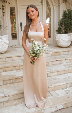 a woman in a long dress holding a flower bouquet standing on some steps with her hands behind her back