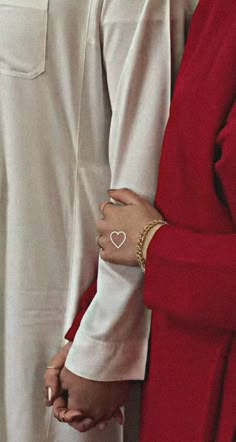 two people are holding hands and wearing red outfits with white hearts on their fingers while standing next to each other