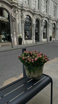 a bunch of flowers sitting on top of a bench next to a building in the city