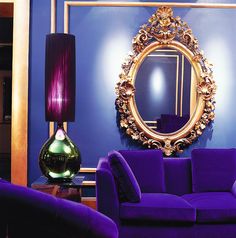 a living room with purple couches and a gold framed mirror on the blue wall