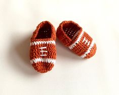 two crocheted baby shoes with white and orange stripes on the soles, sitting on a white surface