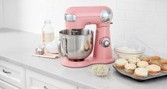 a pink mixer sitting on top of a counter next to cupcakes and muffins