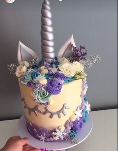 a cake decorated with flowers and a unicorn's horn is being held by a person