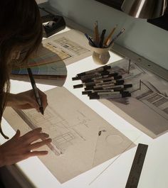 a woman sitting at a table working on architectural drawings and pencils in front of her