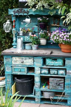 an old blue cabinet with potted plants on top and other flowers in the background