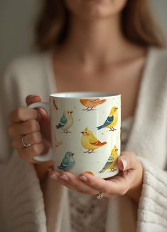 a woman is holding a coffee cup with birds on it and she is wearing a white cardigan