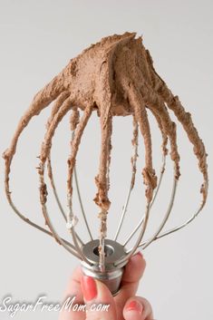 a hand holding a metal whisk with chocolate frosting on the top and bottom