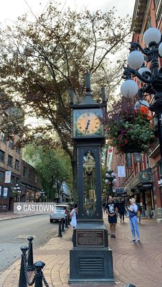 a clock tower on the side of a street with people walking around it and trees in the background