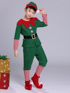 a young boy dressed in an elf costume standing next to a present box and presents