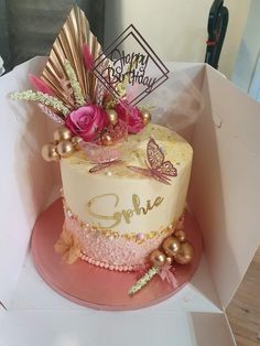 a birthday cake in a box with pink and gold decorations on the top, sitting on a table