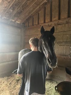 a man standing next to a horse in a barn with hay on the floor and walls