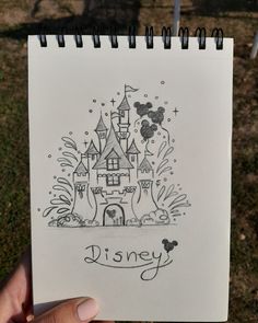 a hand holding up a drawing of a castle with the word disney written on it