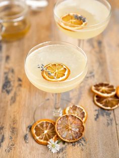 two glasses filled with drinks sitting on top of a wooden table next to sliced oranges