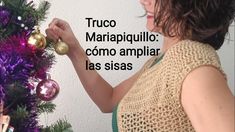 a woman decorating a christmas tree with purple and gold ornaments on it, in front of a white wall